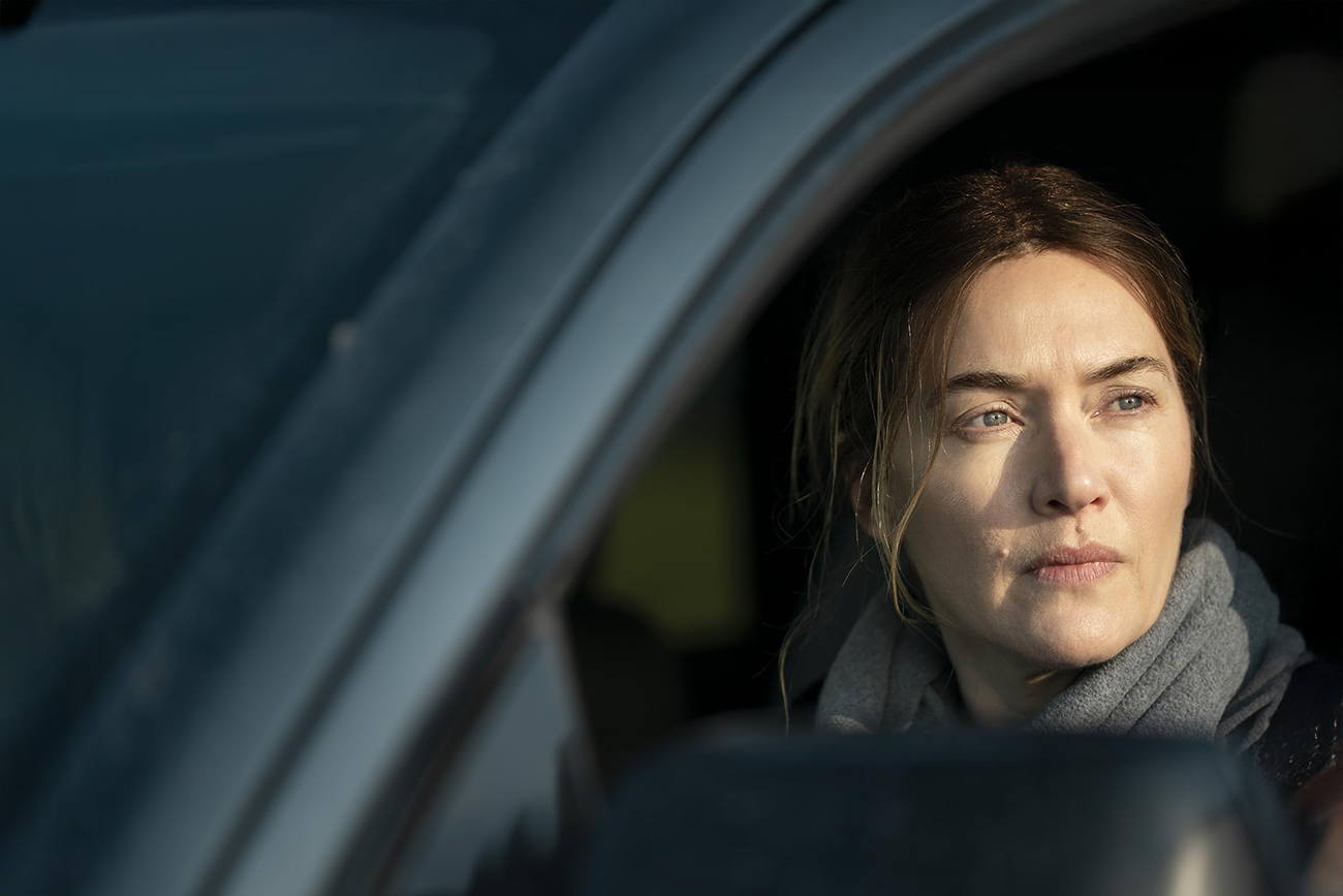 Kate Winslet como Mare Sheehan, dentro de um carro, em Mare of Easttown