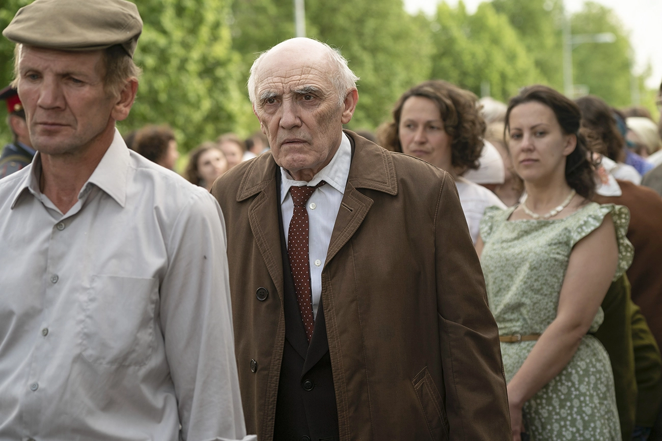 Grupo de moradores reunidos ao ar livre em cena de Chernobyl.