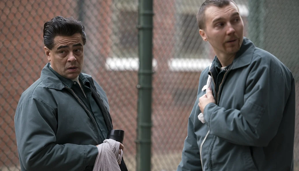Dois homens de uniforme verde junto a uma cerca em cena de Escape at Dannemora.