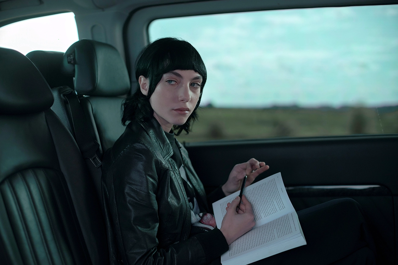 Cena de Irma Vep: mulher de jaqueta preta com um livro aberto no banco de um carro.