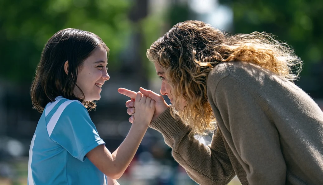 Paula conversa de perto com uma menina de uniforme esportivo em Prazer Máximo Garantido.