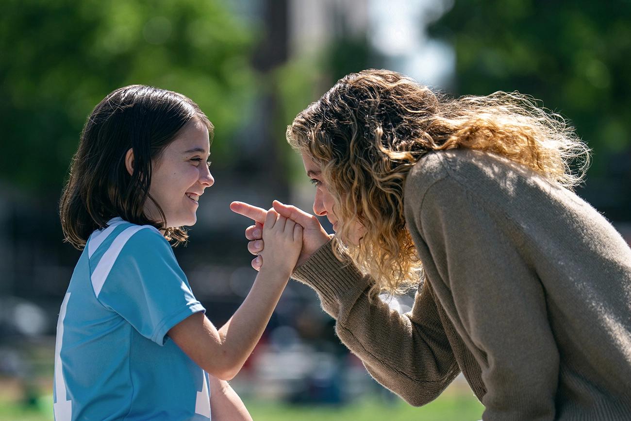 Paula conversa de perto com uma menina de uniforme esportivo em Prazer Máximo Garantido.