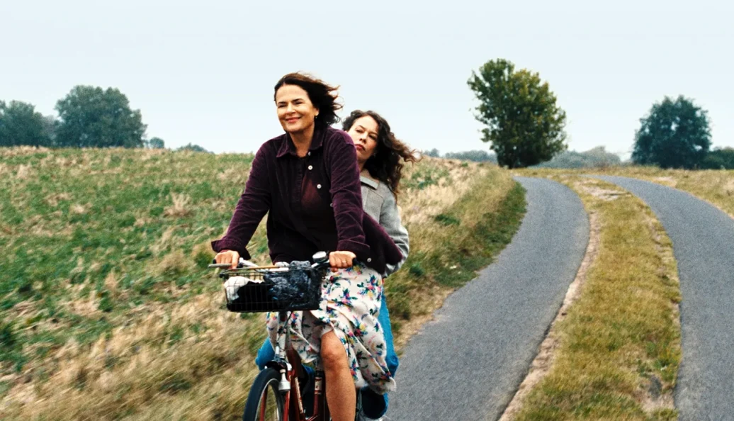 Duas mulheres compartilham uma bicicleta em uma estrada rural em Mirrors No. 3.