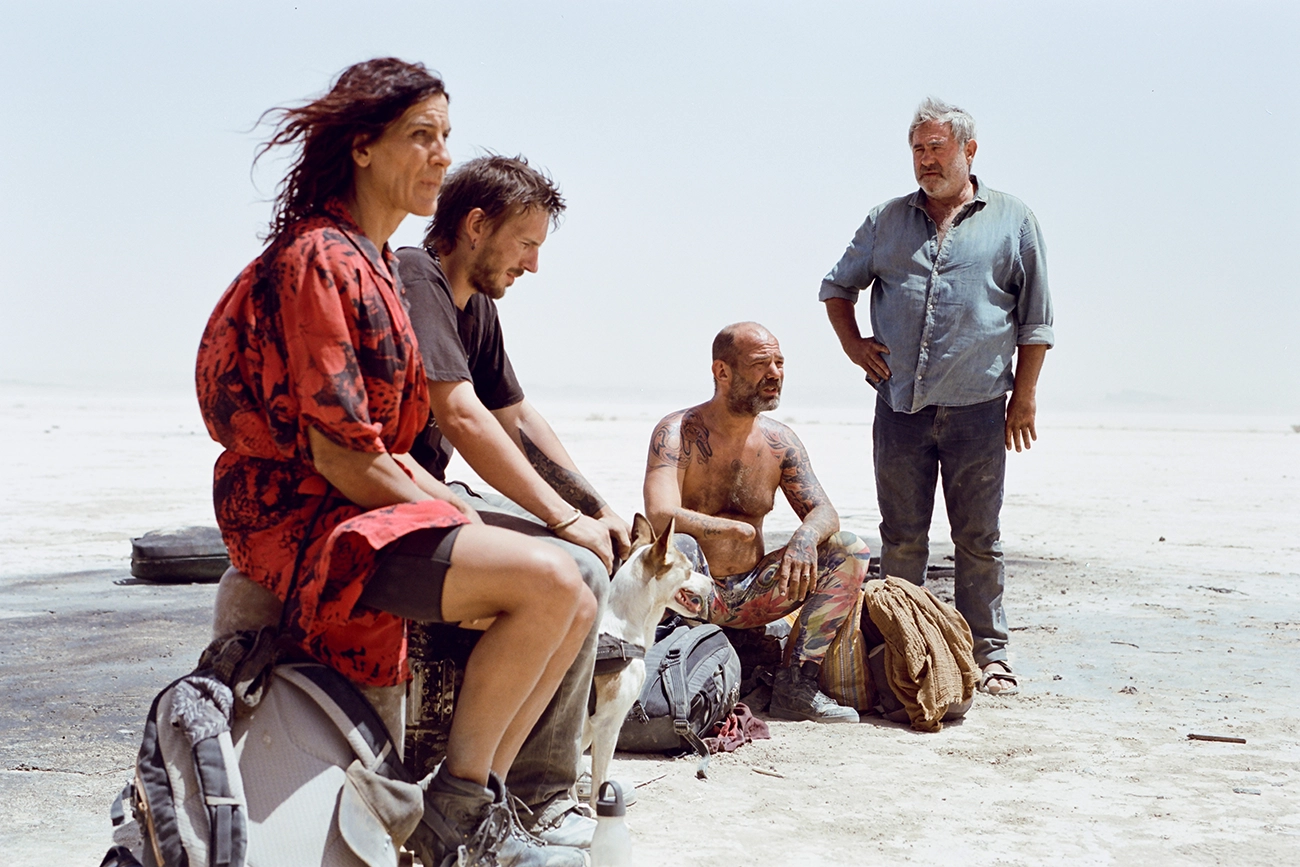 Grupo de viajantes e um cachorro reunidos em uma paisagem desértica em Sirât.