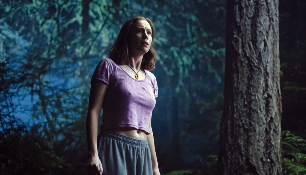 Mulher de camiseta lilás entre árvores em Acampamento Miasma: Adolescência, Sexo e Morte.