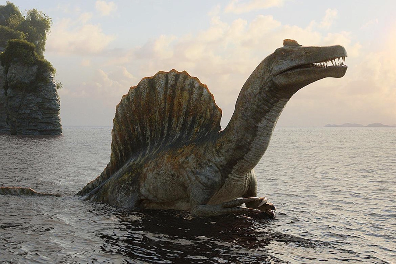 Dinossauro recriado digitalmente emerge da água em cena de Os Dinossauros.