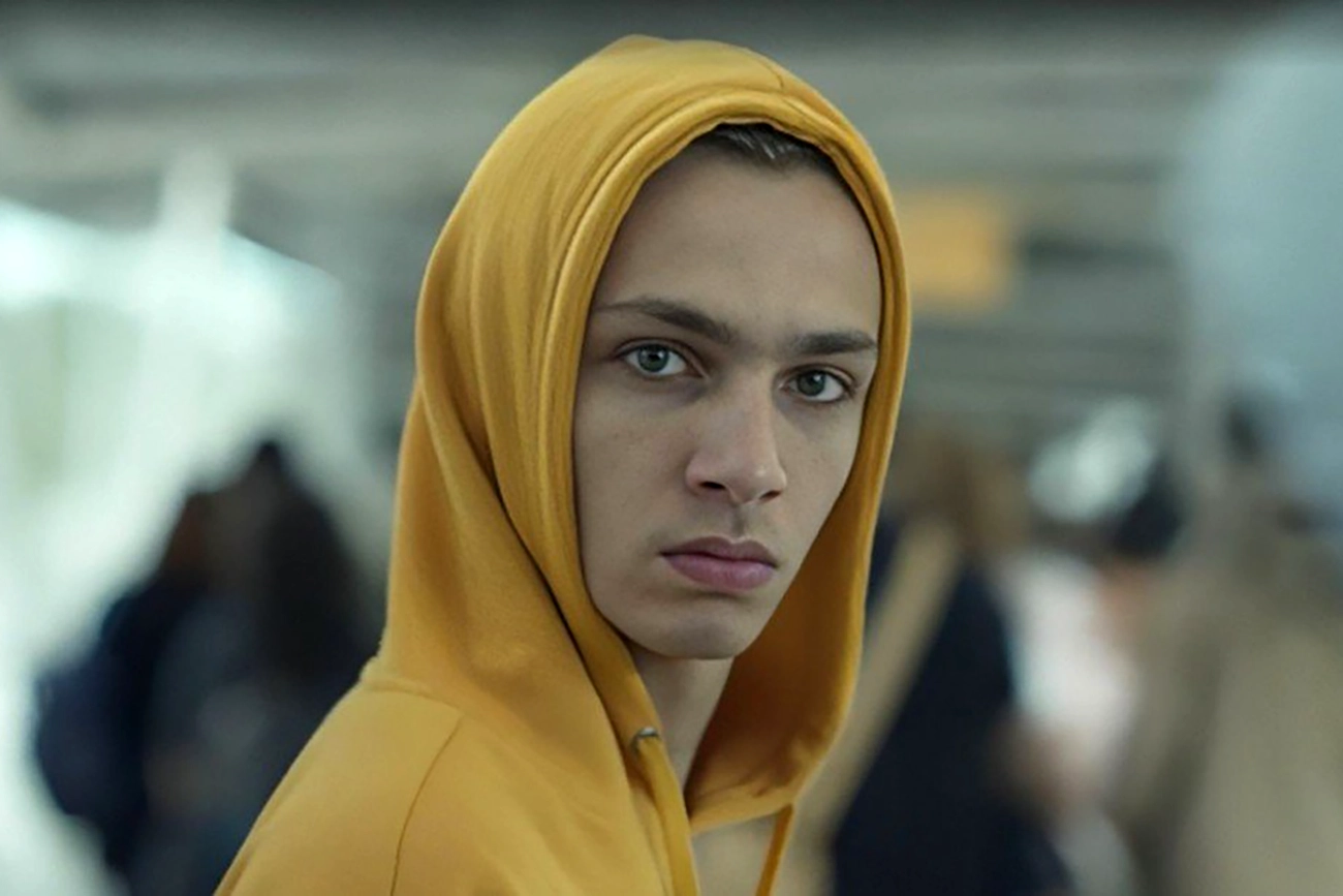 Personagem de Os Outros com capuz amarelo, em meio a uma multidão