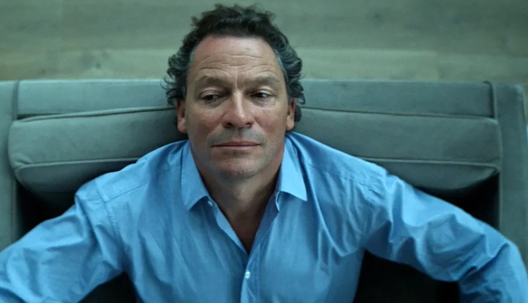 Dominic West sentado em uma poltrona.