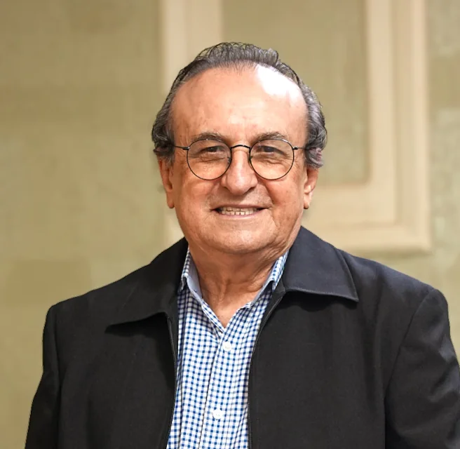 Edival Lourenço sorrindo, de óculos e casaco, em enquadramento do peito para cima.