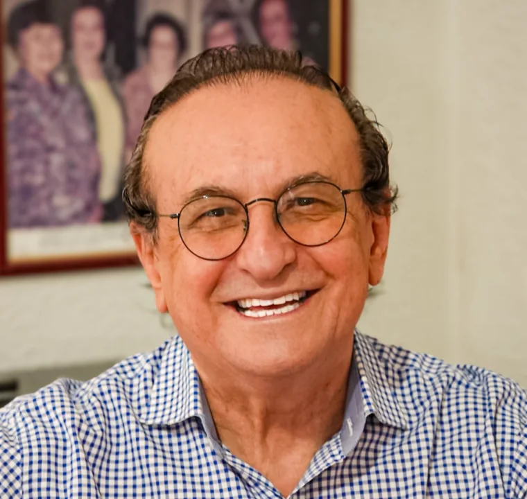 Edival Lourenço sorrindo, de óculos e camisa azul, em retrato do peito para cima.